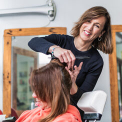 A hairdresser smiles while styling a client's hair in a modern salon. The interaction is friendly and professional. Concept of cheerful salon service.